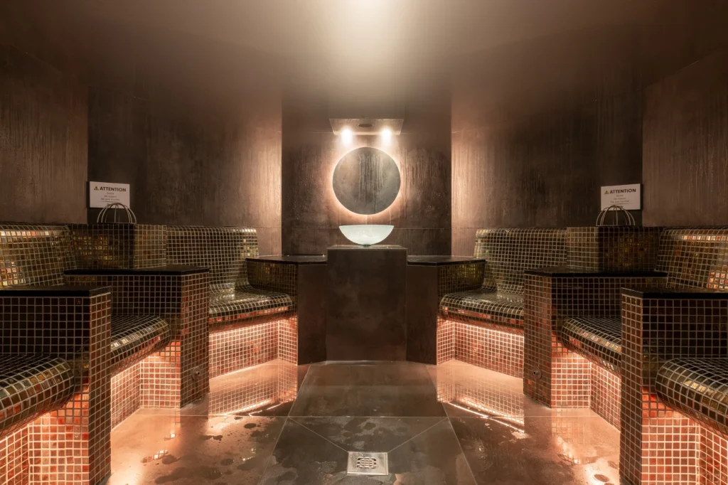Baño turco de un spa con bancos de mosaico y luz cálida en un club deportivo