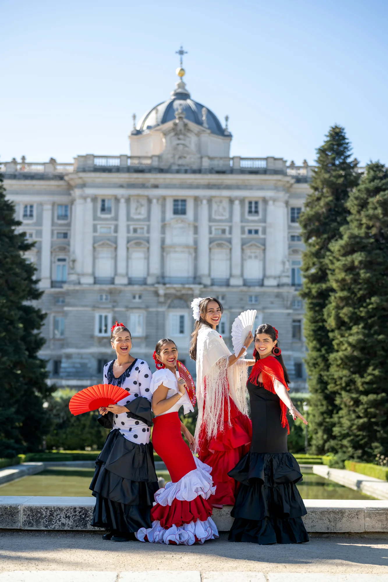 Grupo de mujeres y niñas vestidas de flamenca en los Jardines de Sabatini frente al Palacio Real