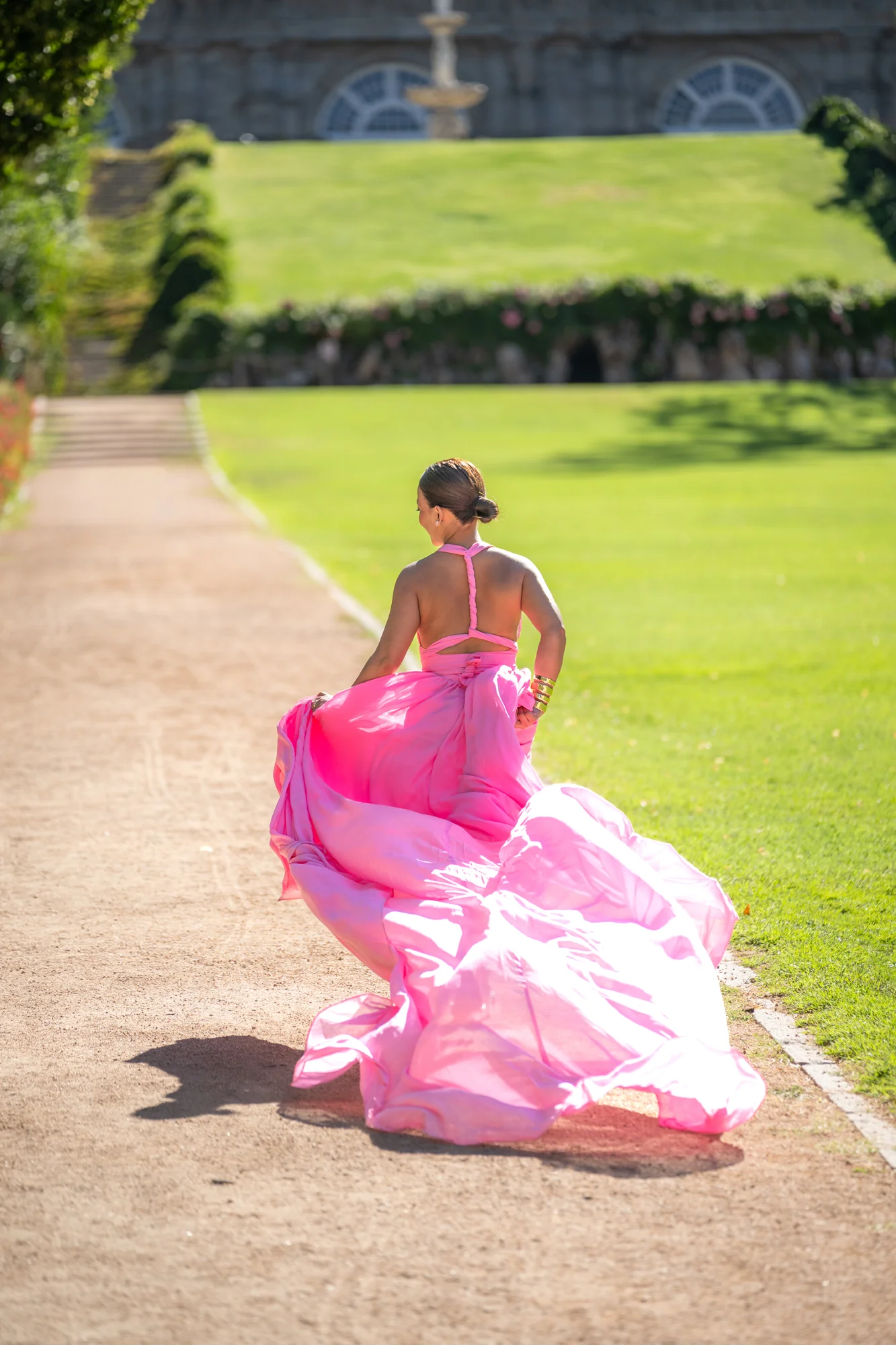 Mujer de espaldas con vestido rosa de cola larga en un camino de los Jardines de Sabatini