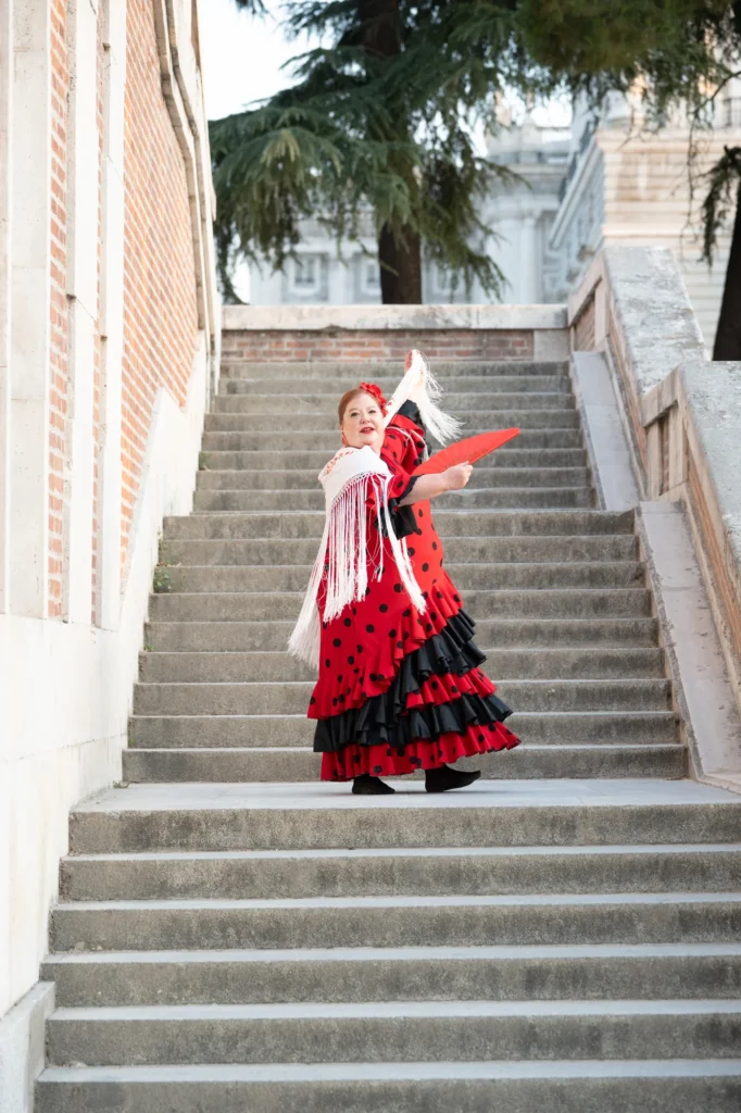 Mujer vestida de flamenca con abanico en lo alto de unas escaleras de piedra en Madrid