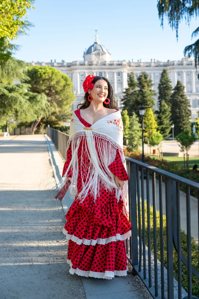 Mujer con traje de flamenca rojo de lunares y mantón blanco en los Jardines de Sabatini con el Palacio Real al fondo