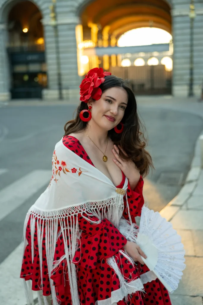 Mujer con traje de flamenca rojo de lunares y mantón blanco bajo un arco de piedra en Madrid