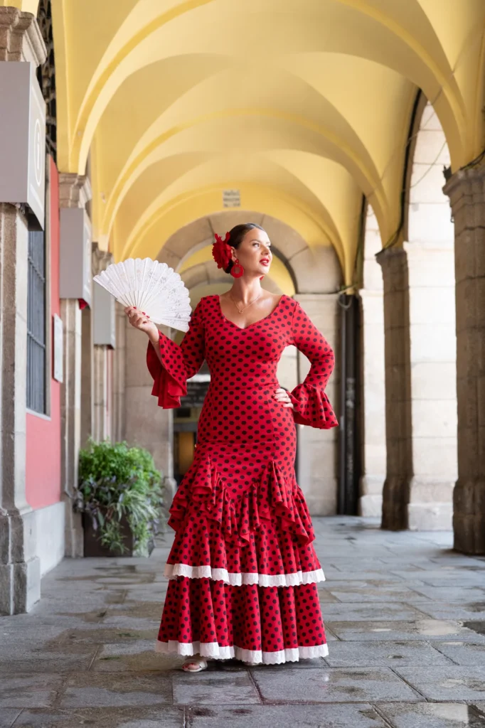 Mujer con vestido de flamenca rojo y abanico blanco bajo unos soportales del centro de Madrid