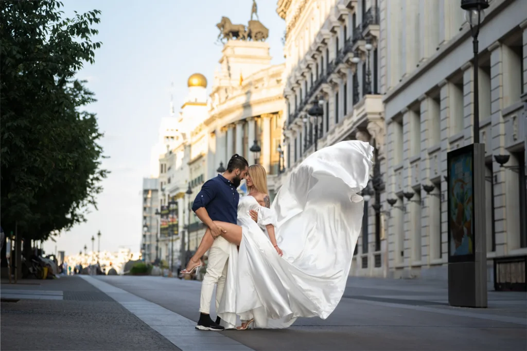 Pareja besándose con un vestido blanco al viento en una calle monumental de Madrid