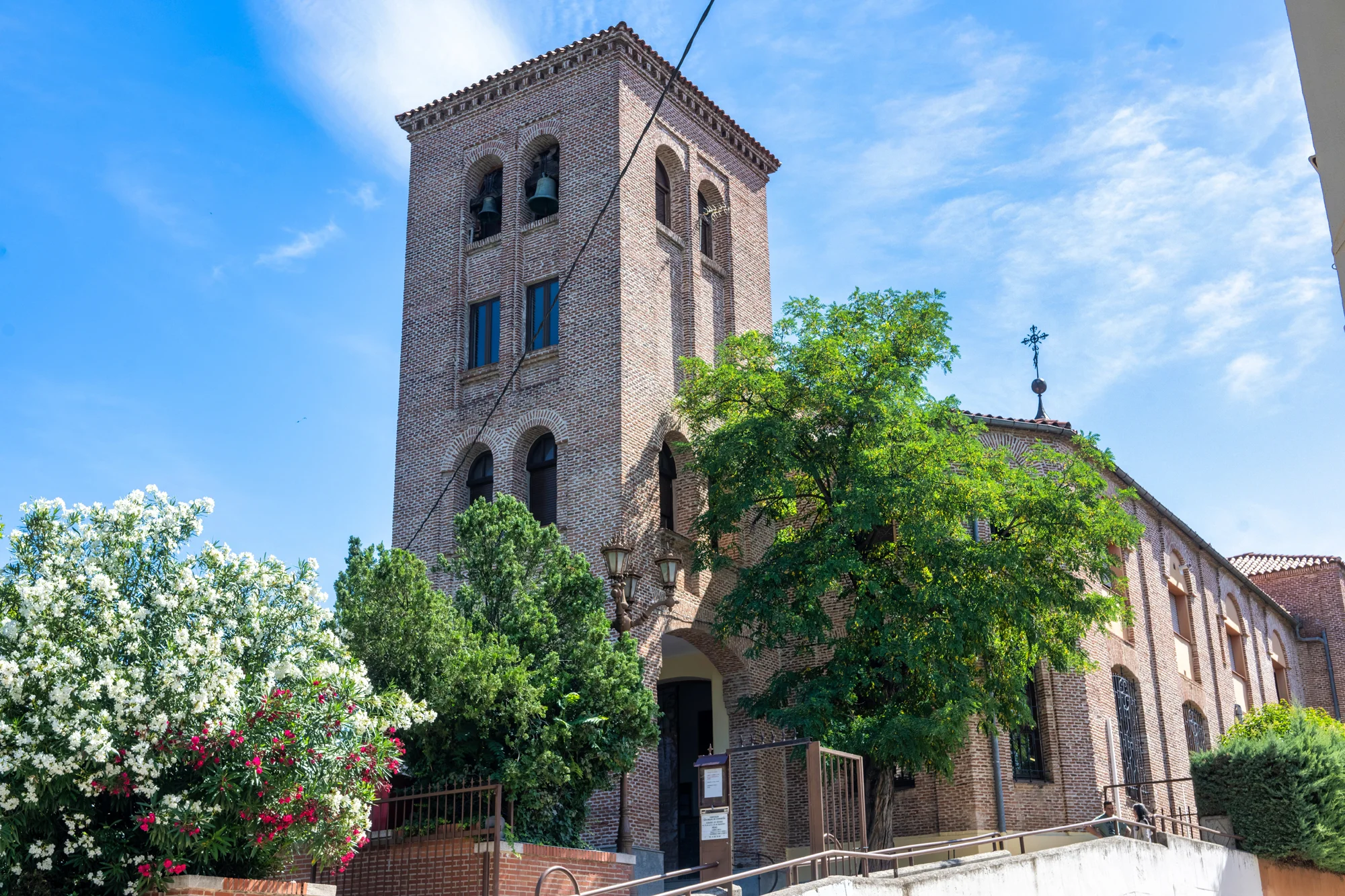 Torre de ladrillo de una iglesia de Madrid rodeada de árboles bajo un cielo azul