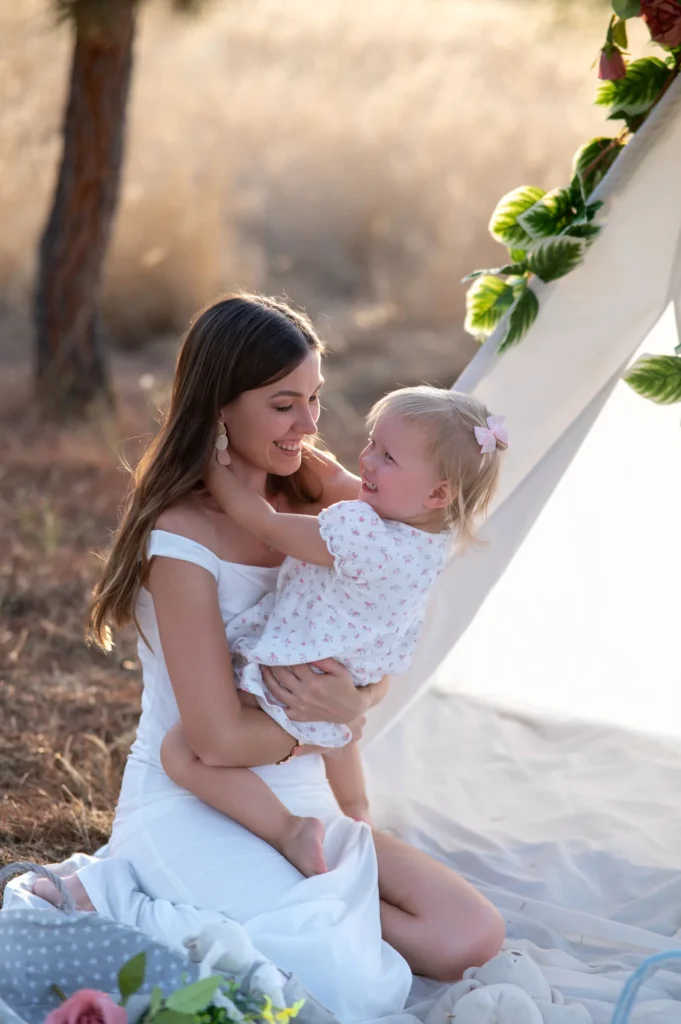 Madre con su bebé en brazos sentada junto a un tipi blanco al atardecer