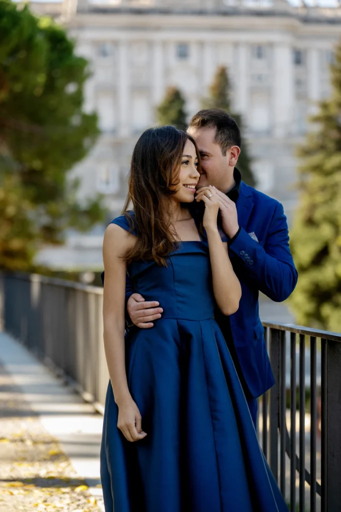 Pareja abrazada junto a una barandilla con el Palacio Real de fondo y luz dorada