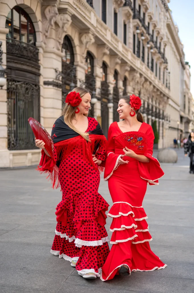 Dos mujeres con trajes de flamenca rojos de lunares paseando por una calle del centro de Madrid