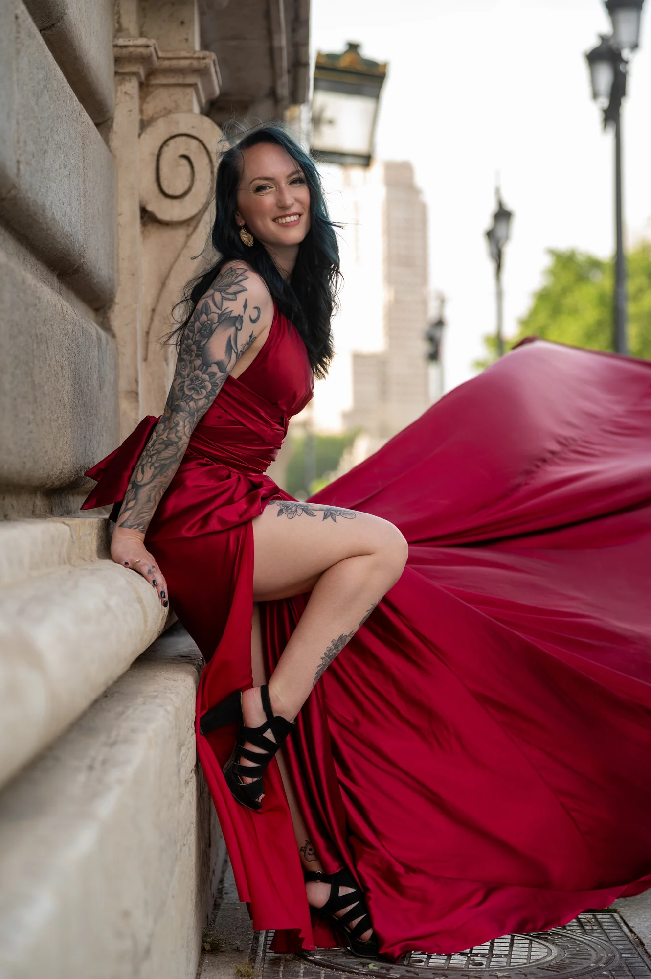 Mujer tatuada con vestido rojo sentada en un pedestal de piedra con la cola al viento