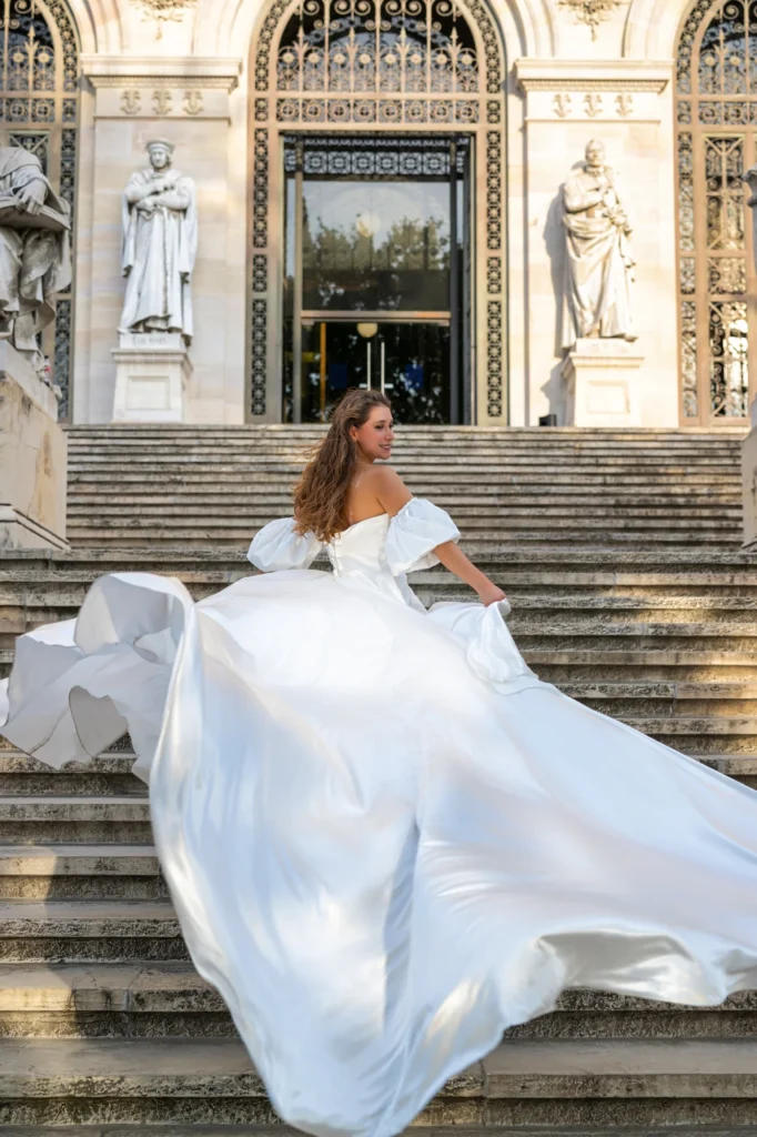 Mujer con vestido blanco de cola larga bajando una escalinata con estatuas en Madrid
