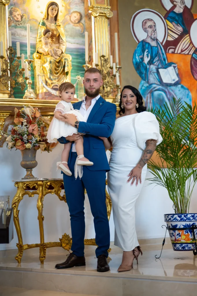 Padres posando con su bebé frente al altar dorado de una iglesia tras el bautizo