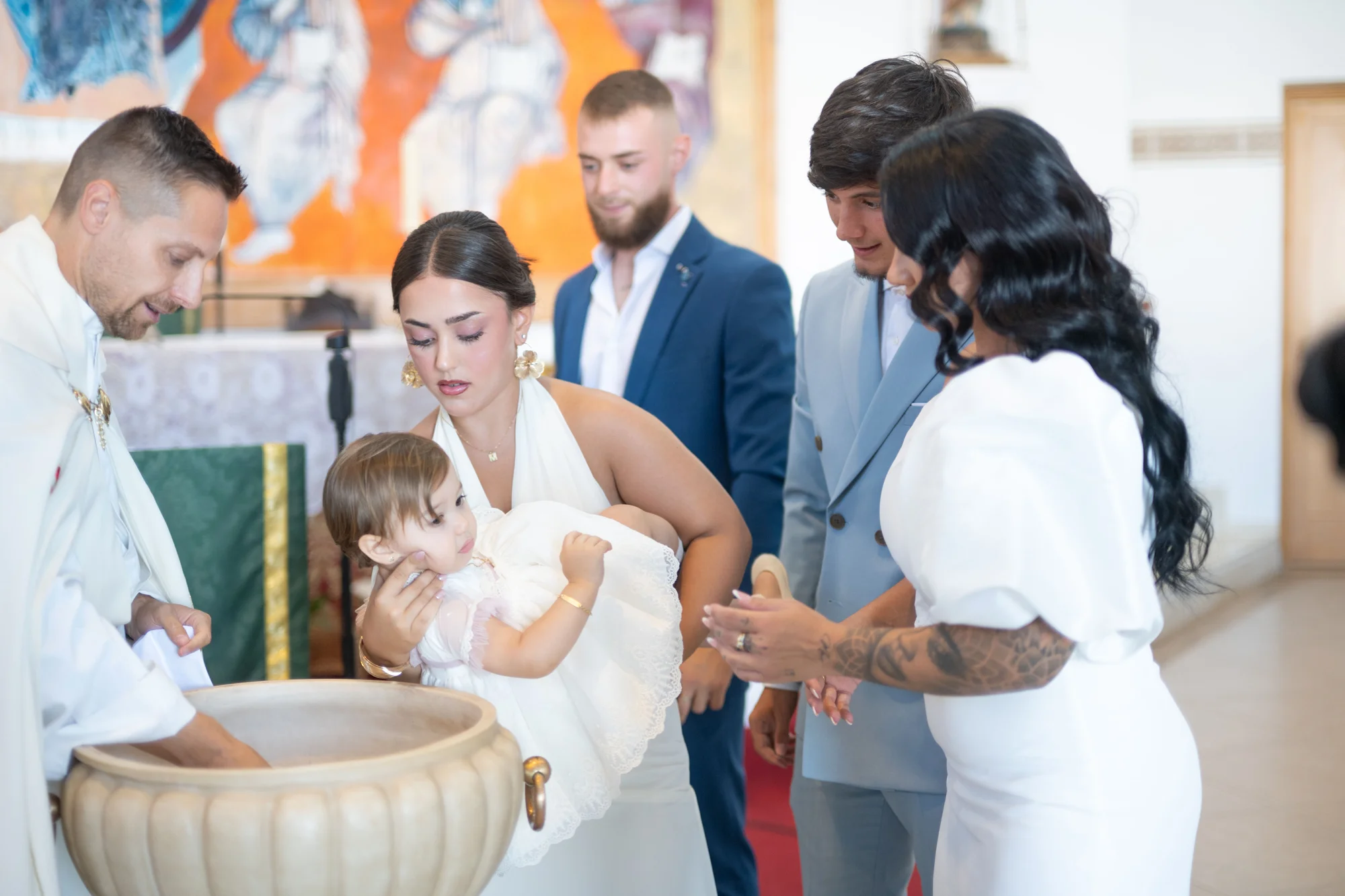 Familia rodeando la pila bautismal mientras el sacerdote bautiza a la bebé