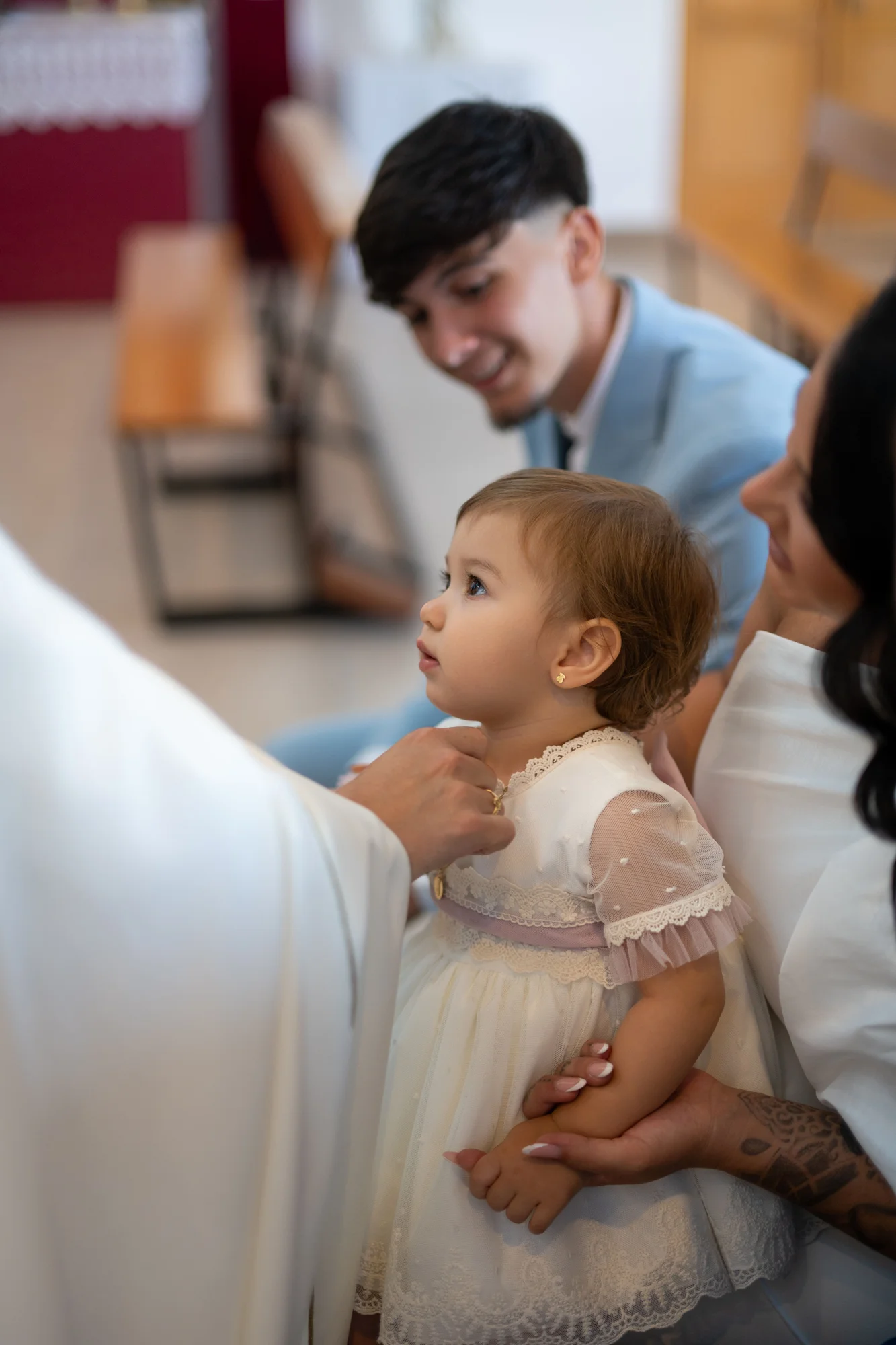 Bebé con vestido blanco mirando a su padre durante la ceremonia de bautizo