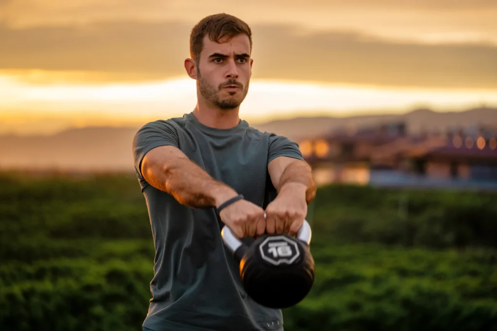 Hombre levantando una kettlebell al atardecer con la ciudad de fondo