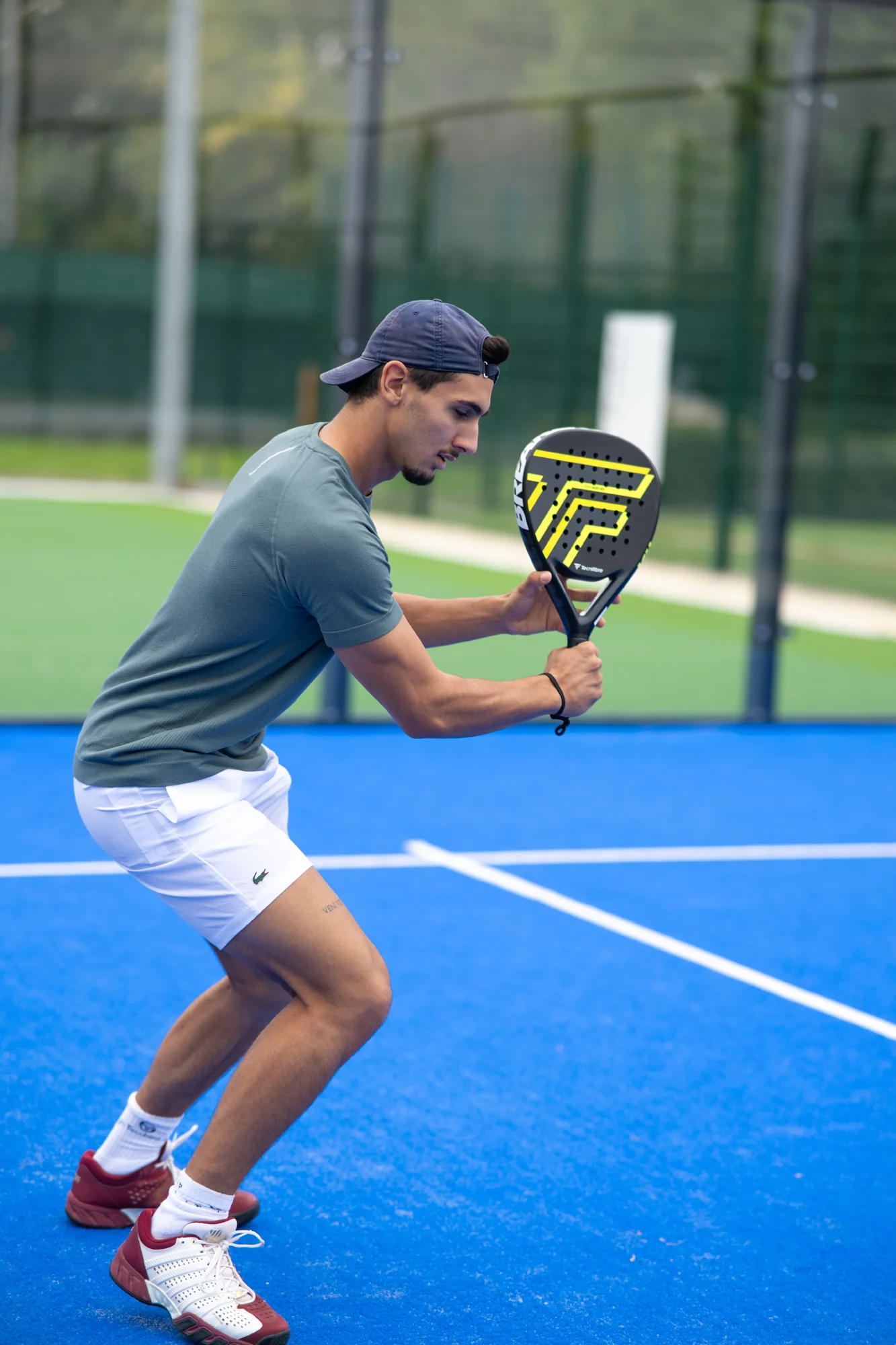 Jugador de pádel con gorra preparando un golpe de derecha en una pista azul