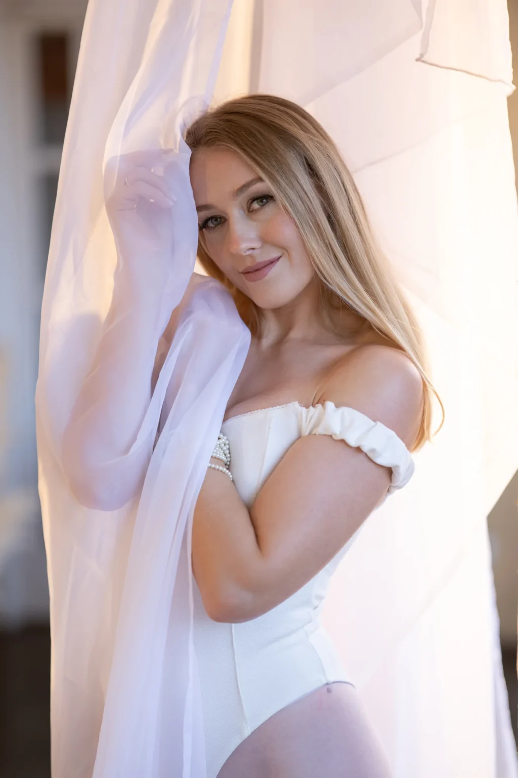 Modelo con body blanco envuelta en una cortina de gasa junto a la ventana