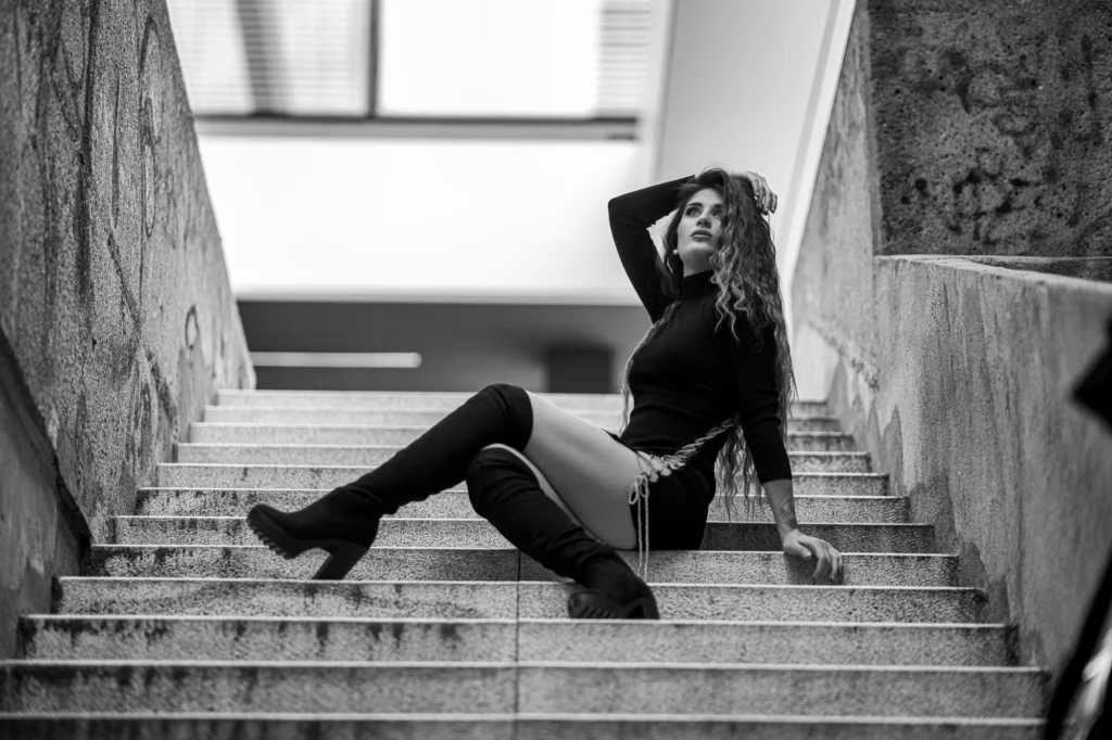 Modelo con ropa negra y botas sentada en unas escaleras en blanco y negro