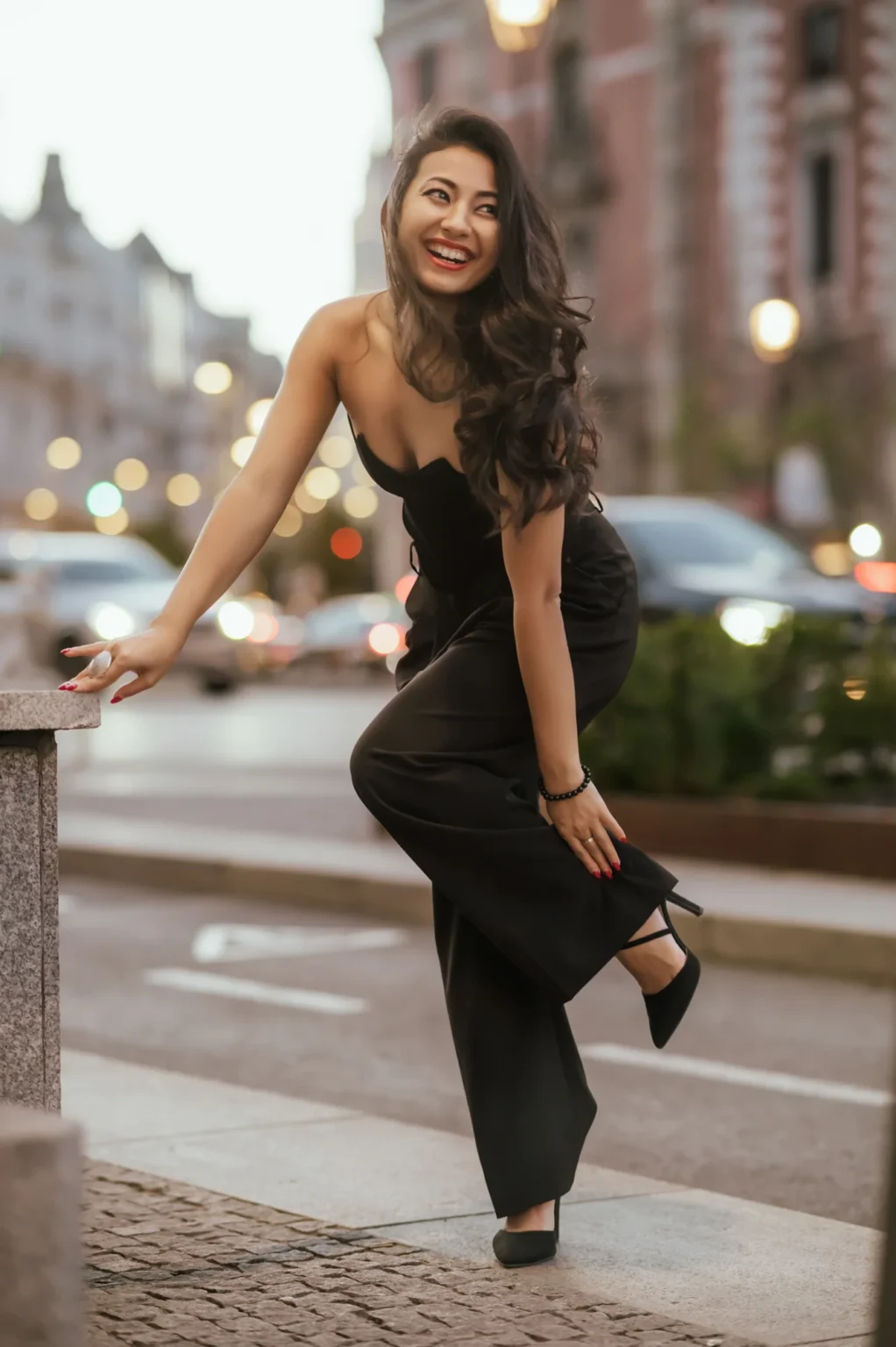 Modelo sonriente con mono negro apoyada en un poste de piedra en una calle de Madrid
