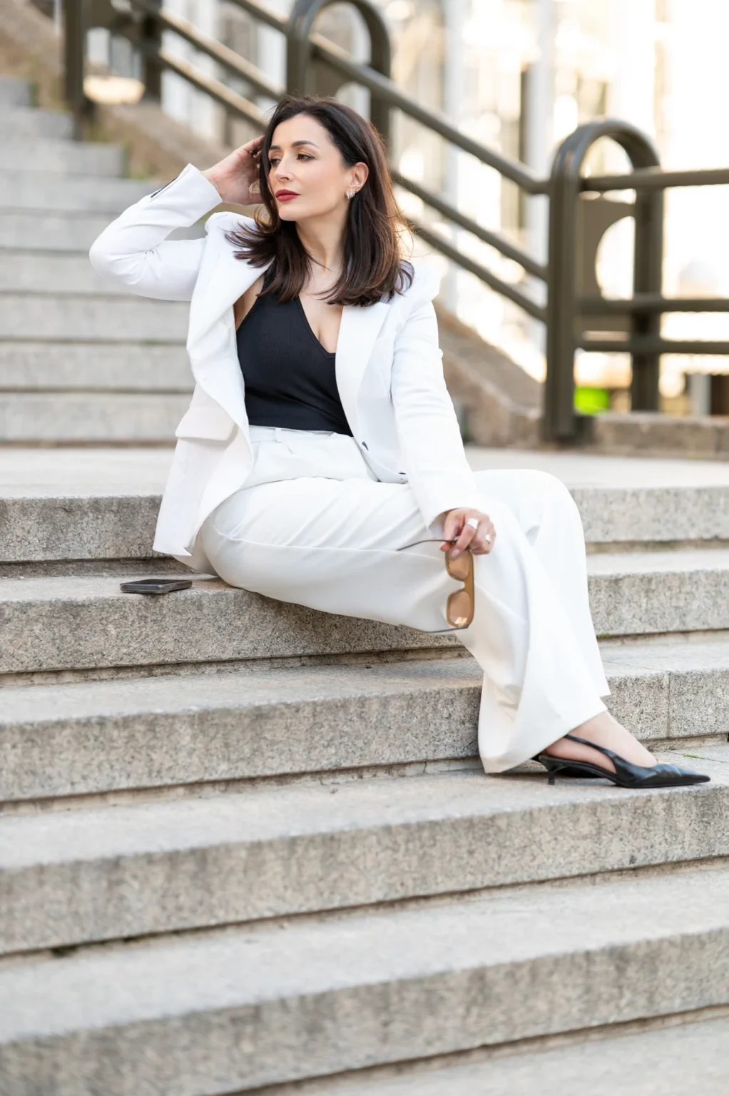 Modelo con traje blanco sentada en unas escaleras de piedra con barandilla