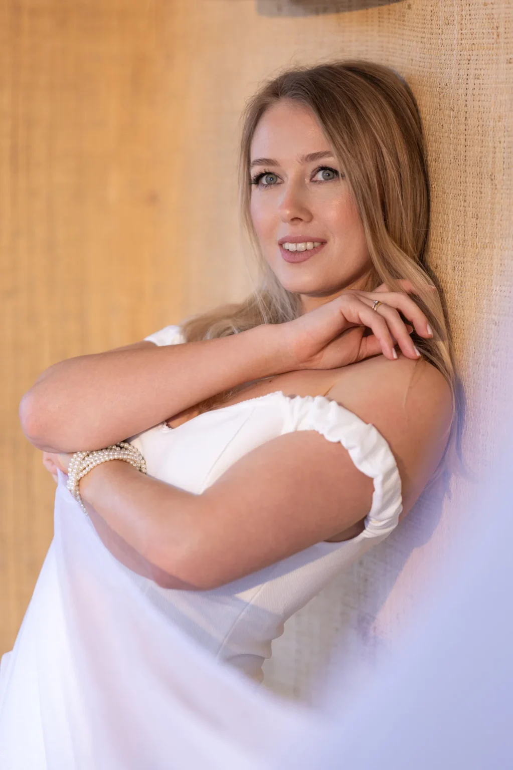 Modelo con vestido blanco apoyada en una pared de textura cálida