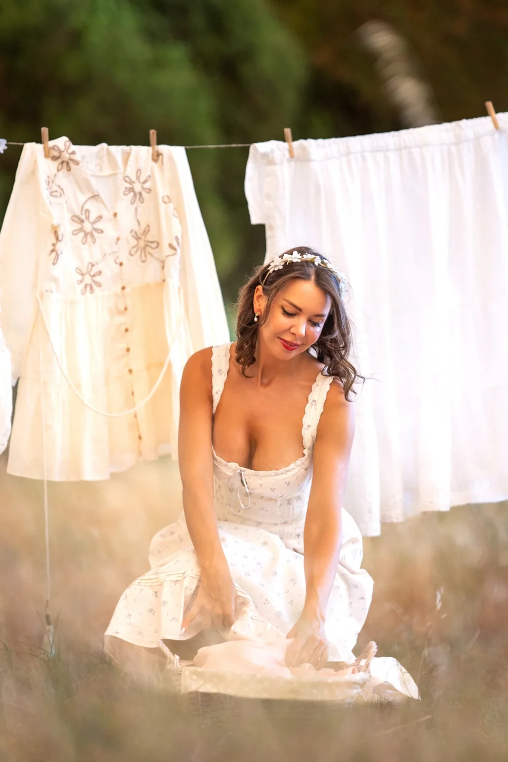 Modelo con vestido blanco de estilo vintage lavando ropa junto a un tendedero en el campo