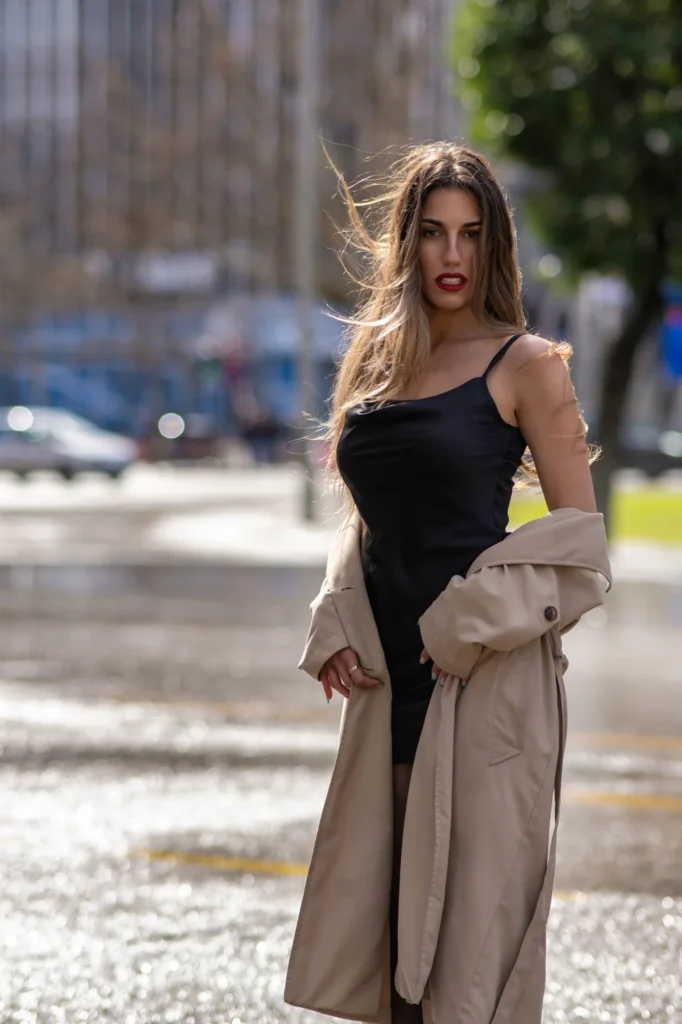Modelo con vestido negro y gabardina beige en una calle mojada de Madrid