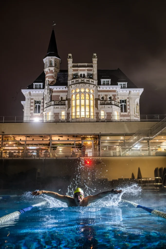 Nadador en la piscina exterior iluminada de noche frente al edificio histórico de un club deportivo