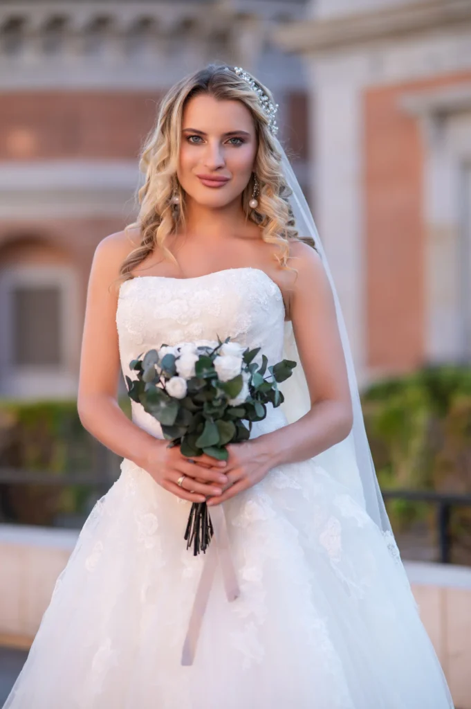Novia con vestido palabra de honor y ramo de rosas blancas en un patio