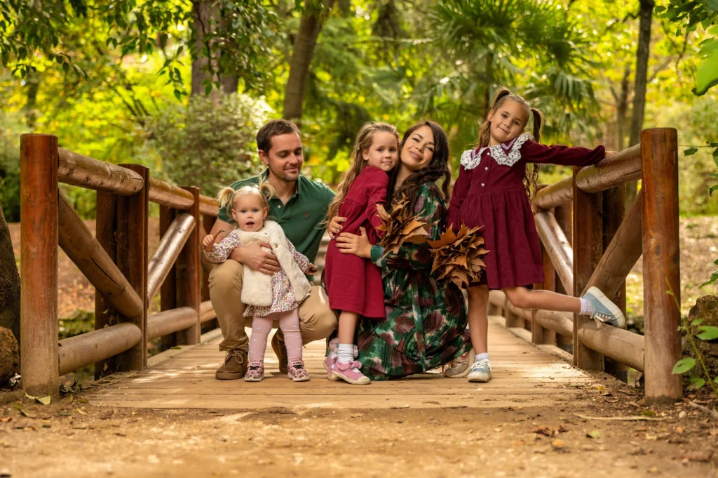 Familia con tres niñas sentada en un puente de madera rodeado de árboles