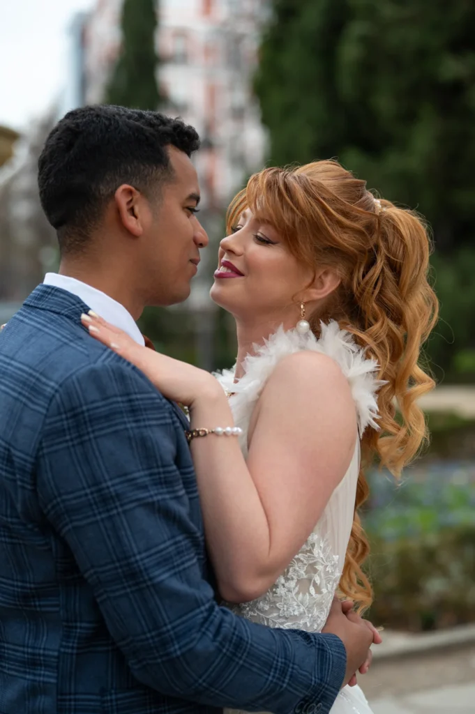Pareja a punto de besarse, ella pelirroja con vestido de plumas, en un jardín