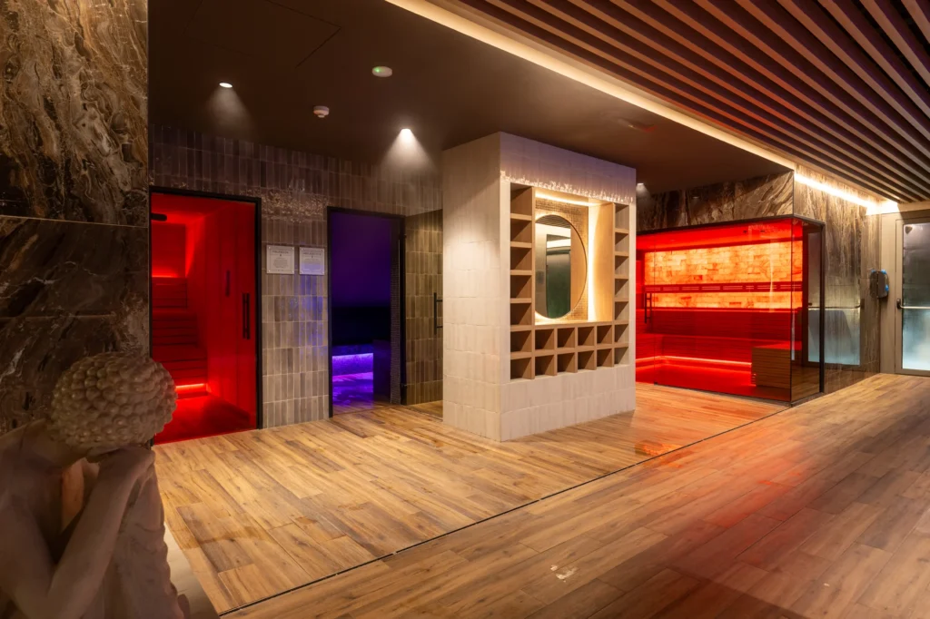 Pasillo del spa con suelo de madera, saunas iluminadas y techo de listones