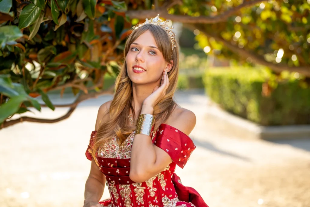 Quinceañera con vestido rojo y corona bajo un magnolio en un jardín de Madrid