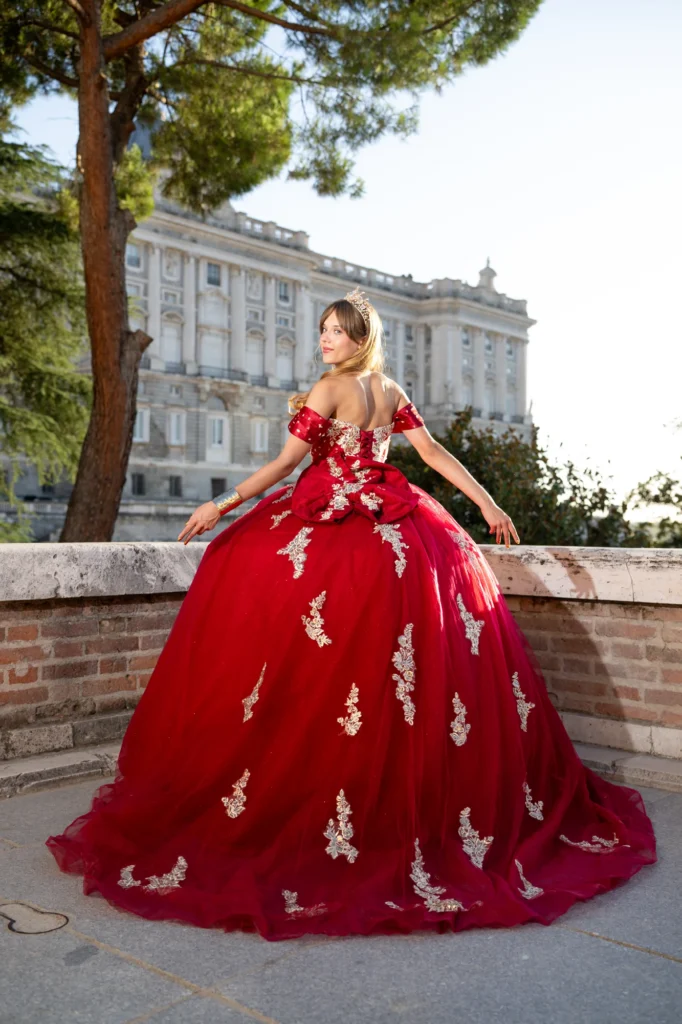 Quinceañera con vestido rojo de gala apoyada en un muro frente al Palacio Real