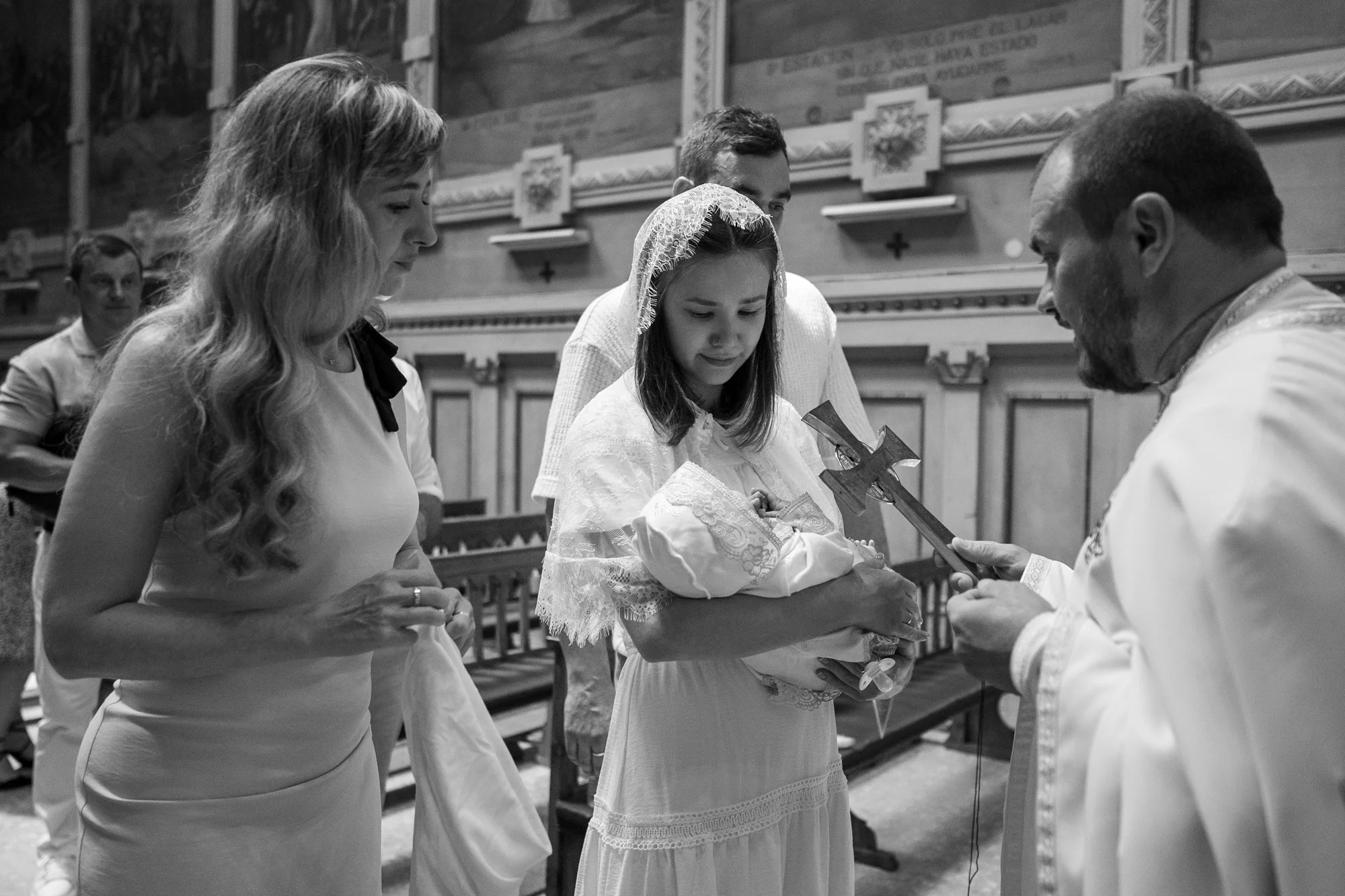 Momento del bautizo en blanco y negro con los padres y el sacerdote junto a la pila