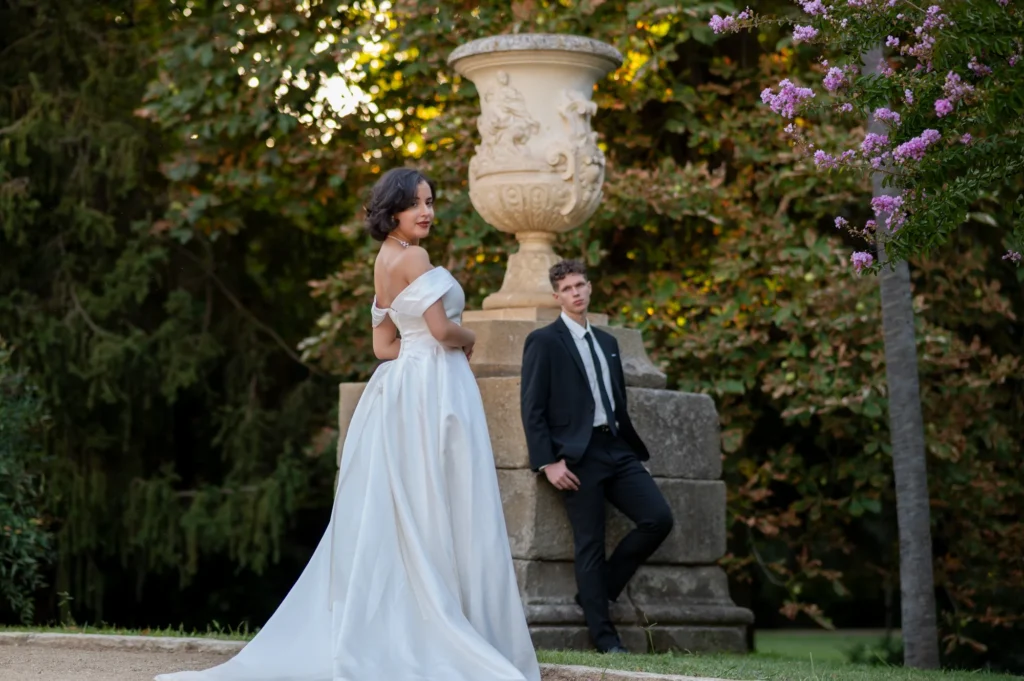 Novios posando junto a un jarrón de piedra en un jardín al atardecer