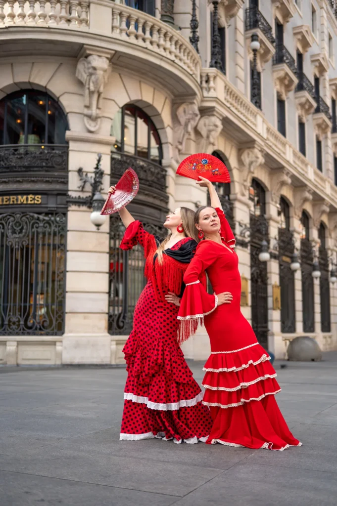 Dos mujeres con trajes de flamenca rojos y abanicos posando ante un edificio histórico de Madrid