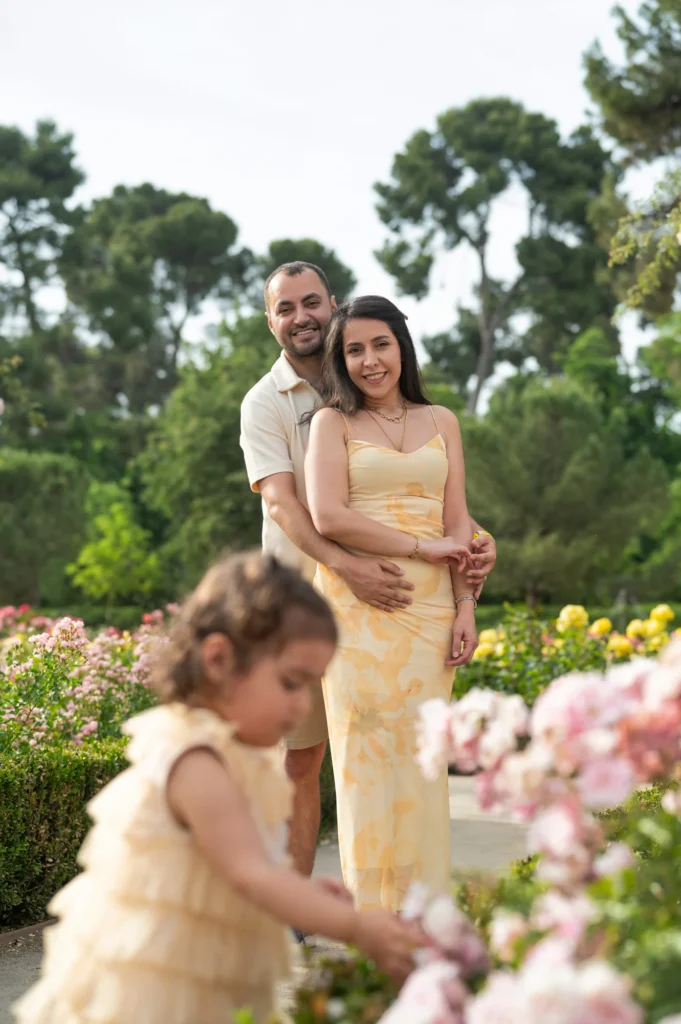 Padres abrazados mirando a su hija entre rosales en un jardín