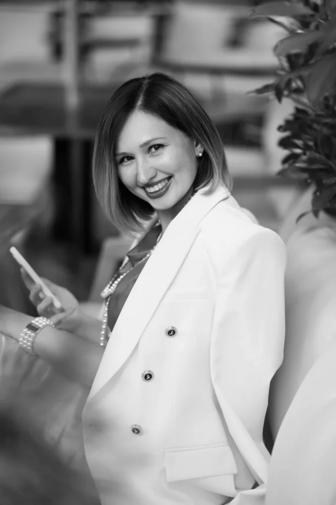 Retrato en blanco y negro de una mujer con blazer blanco mirando su móvil y sonriendo