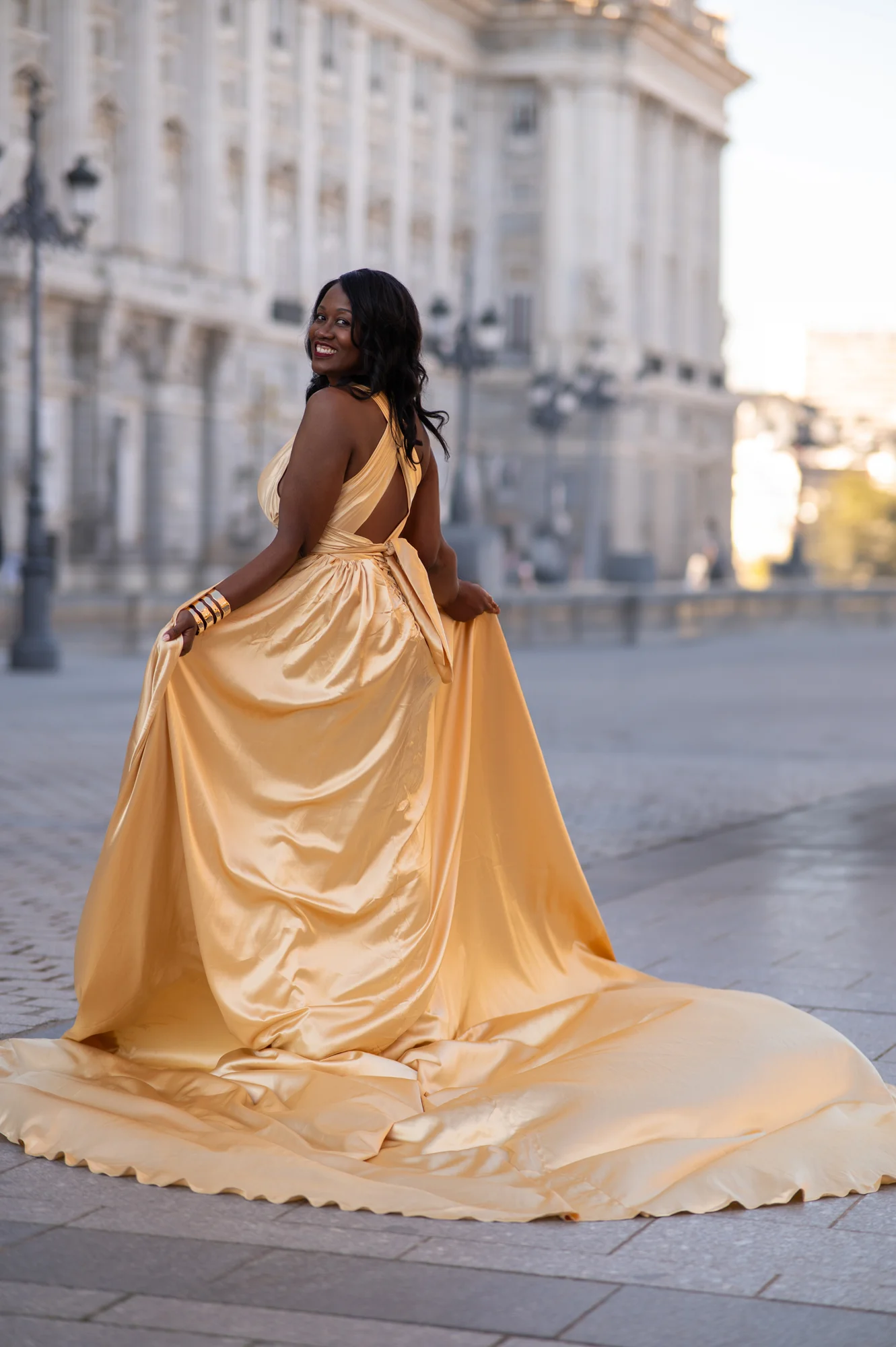 Mujer con vestido dorado de cola larga de espaldas en una calle junto al Palacio Real