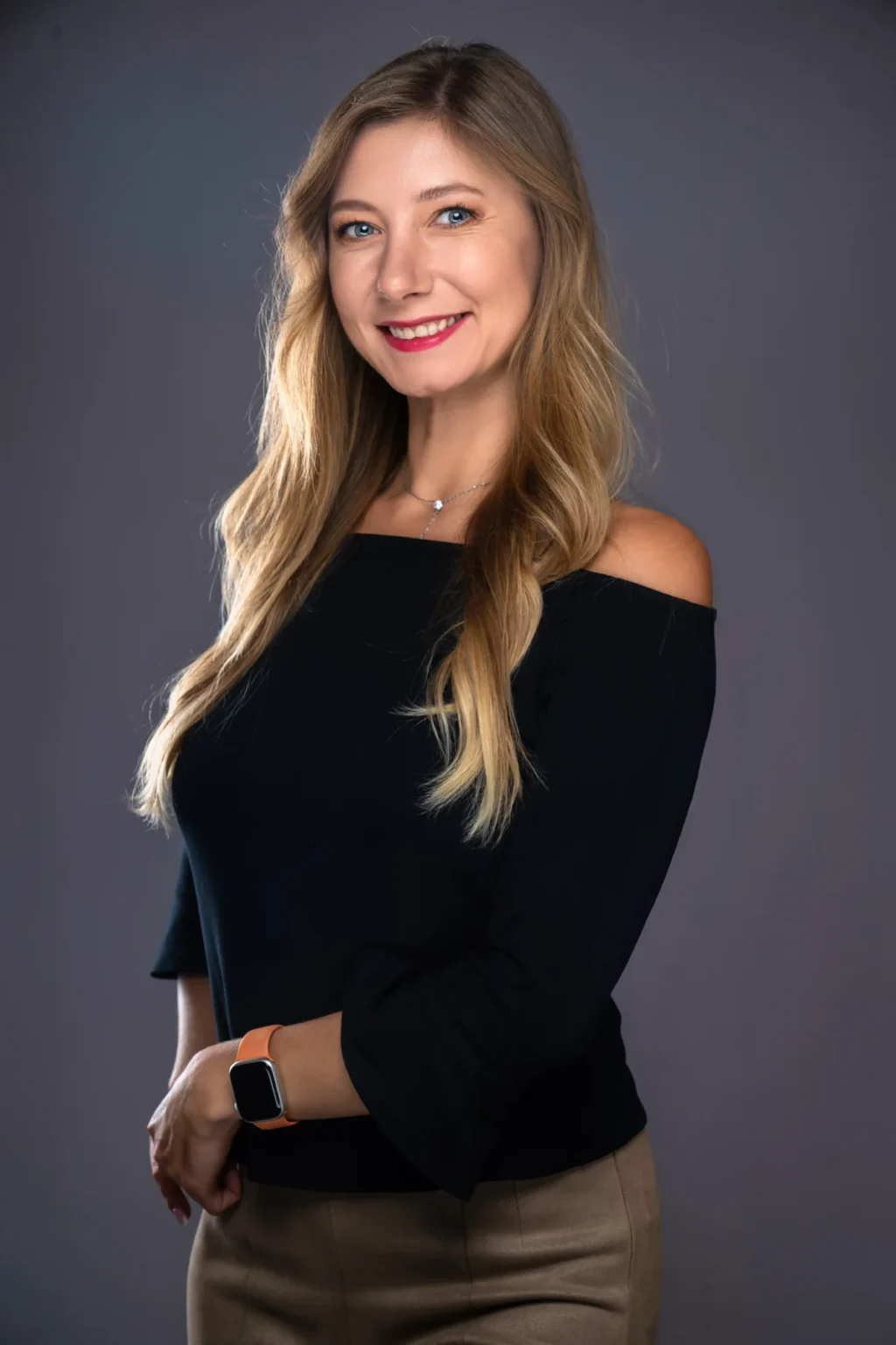 Retrato de una mujer sonriente con jersey negro de hombros descubiertos sobre fondo gris