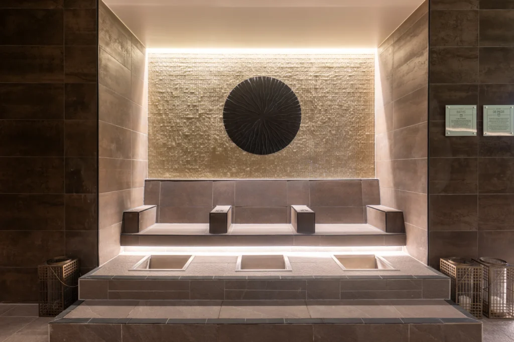 Sala de vapor de un spa con bancos de piedra y un disco decorativo iluminado en la pared