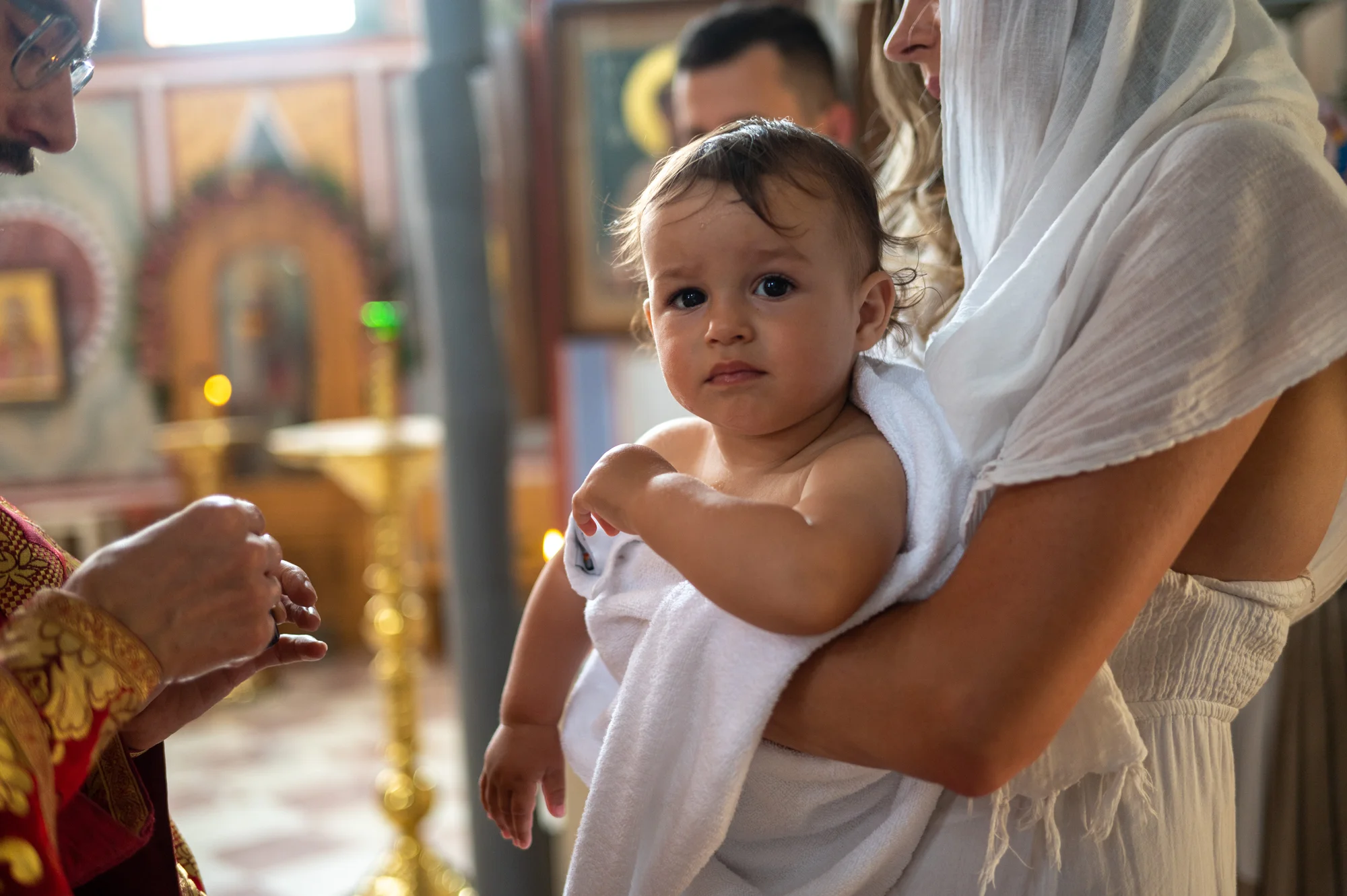 Madre con pañuelo blanco sosteniendo a su bebé en una iglesia ortodoxa durante el bautizo