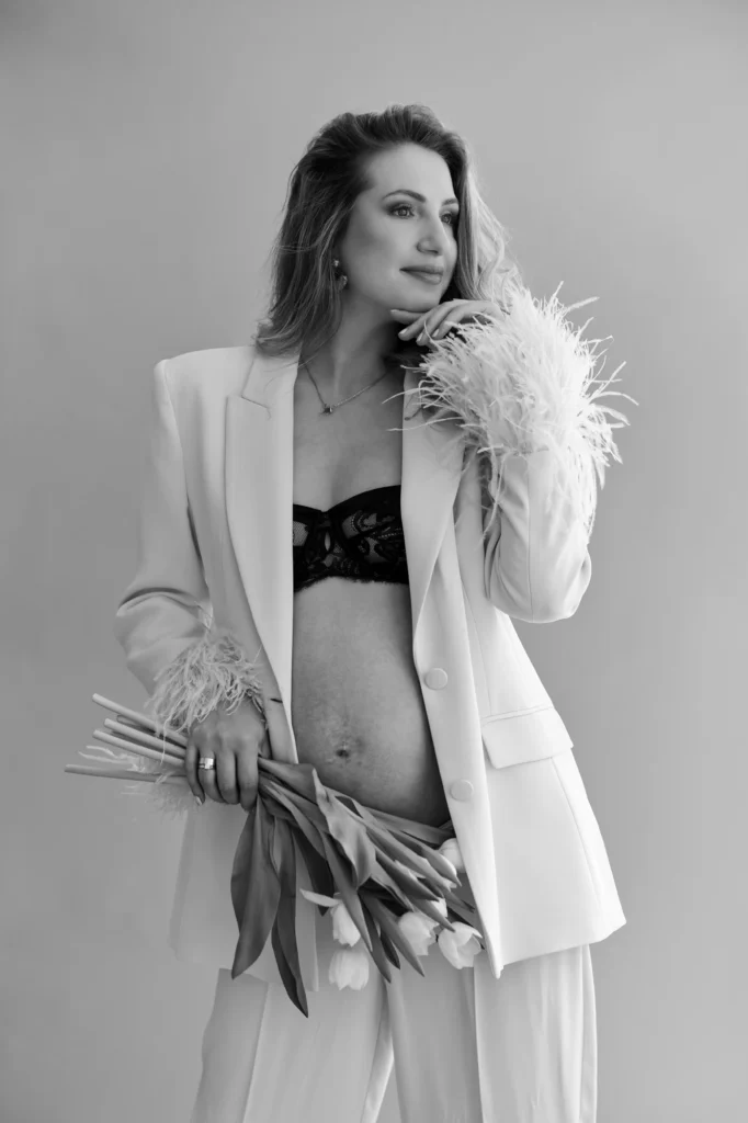 Embarazada con blazer blanco de plumas y ramo de flores en blanco y negro