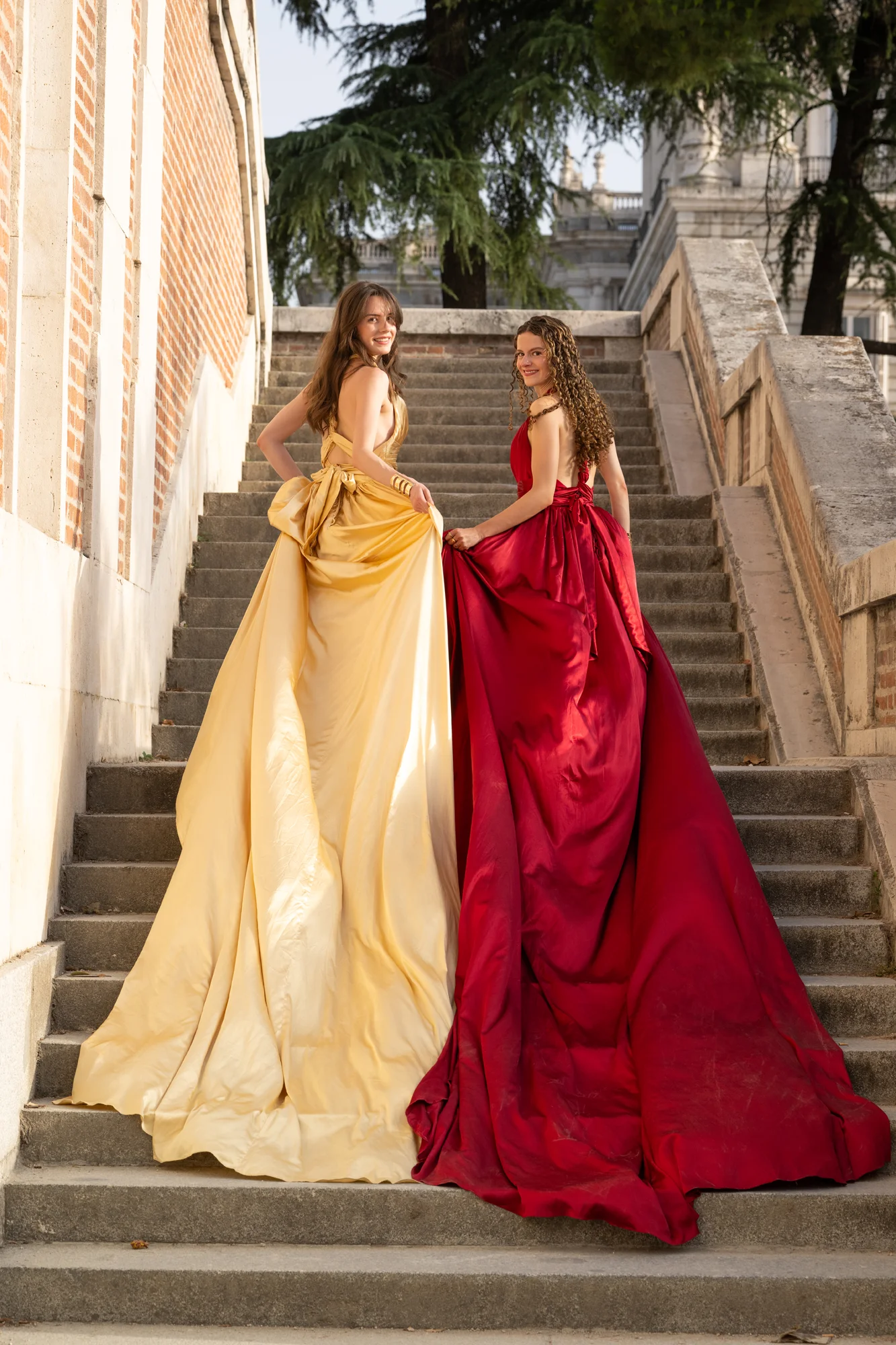 Dos mujeres con vestidos amarillo y rojo de cola larga en una escalinata de piedra