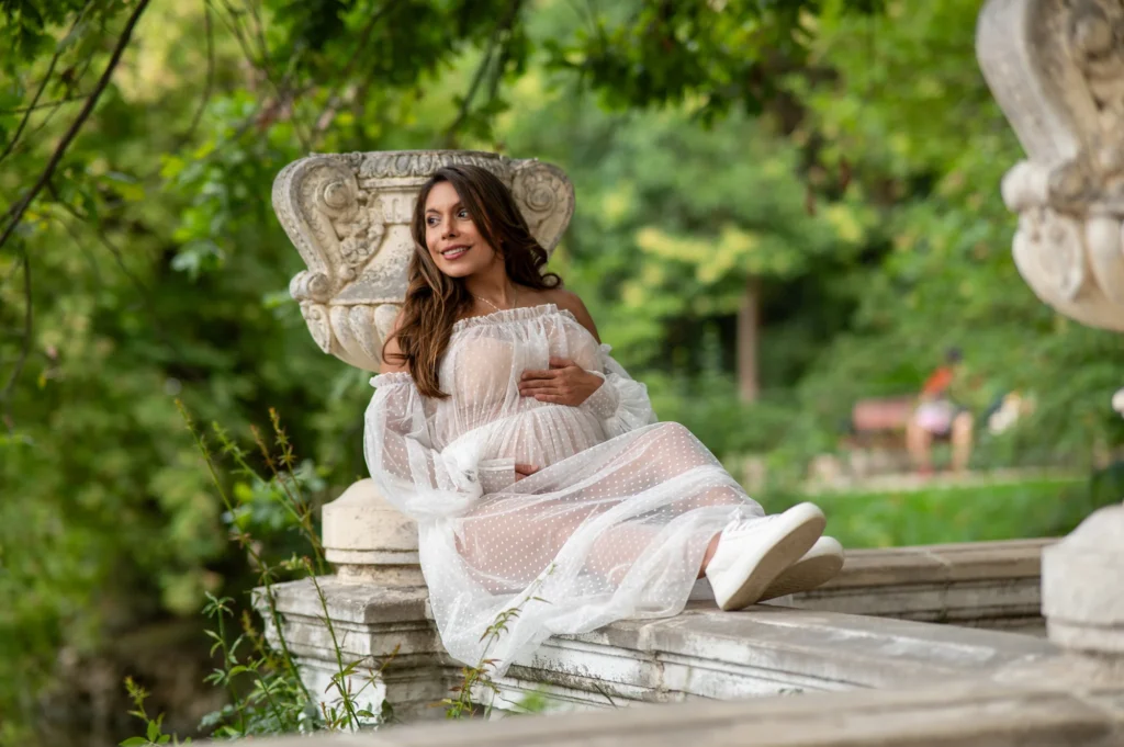 Embarazada con vestido blanco de tul recostada en una fuente de piedra del Parque del Retiro