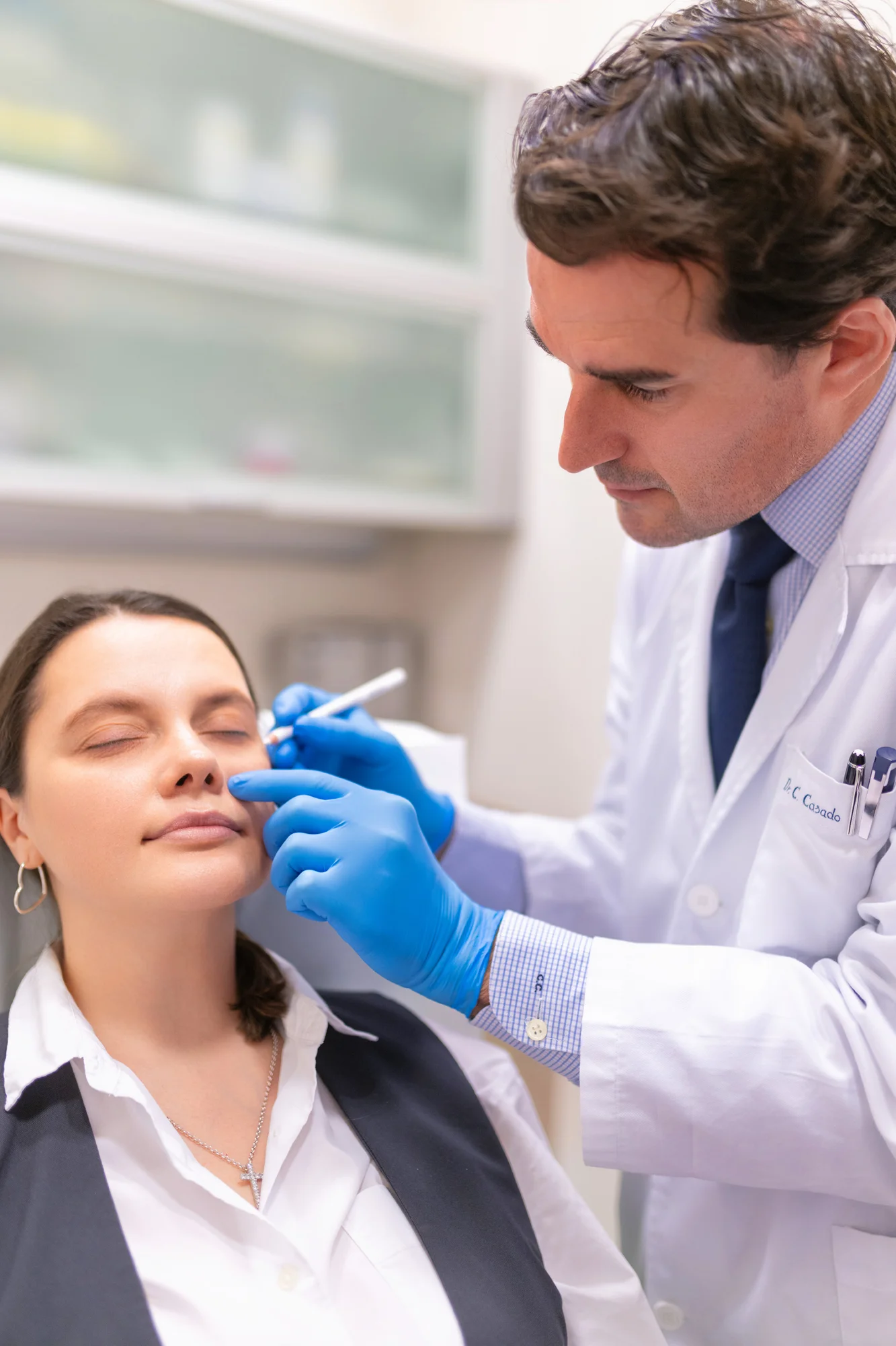 Médico con bata blanca y guantes azules atendiendo a una paciente en una sesión de marca personal