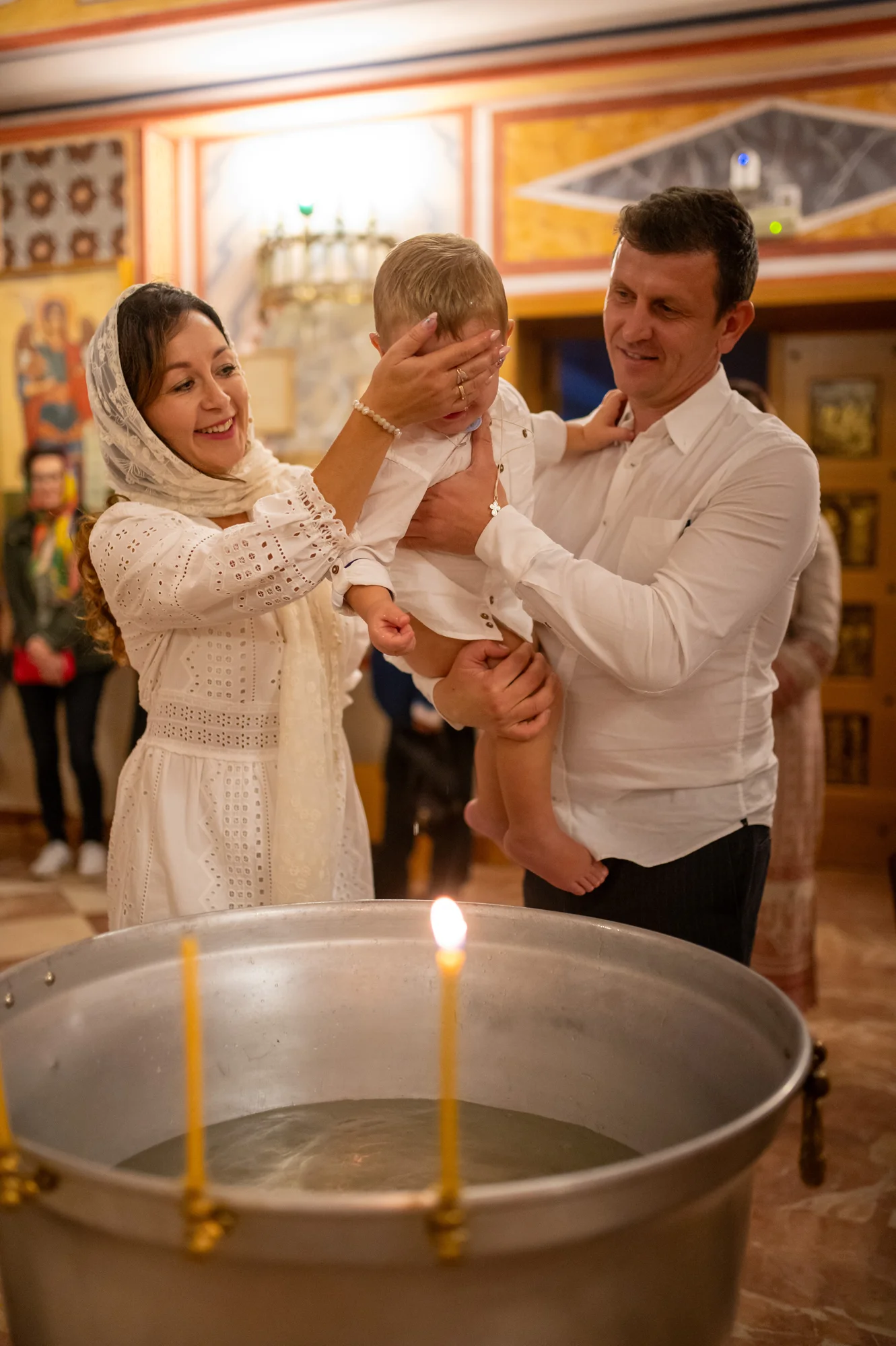 Padres levantando a su bebé junto a la pila bautismal con velas encendidas