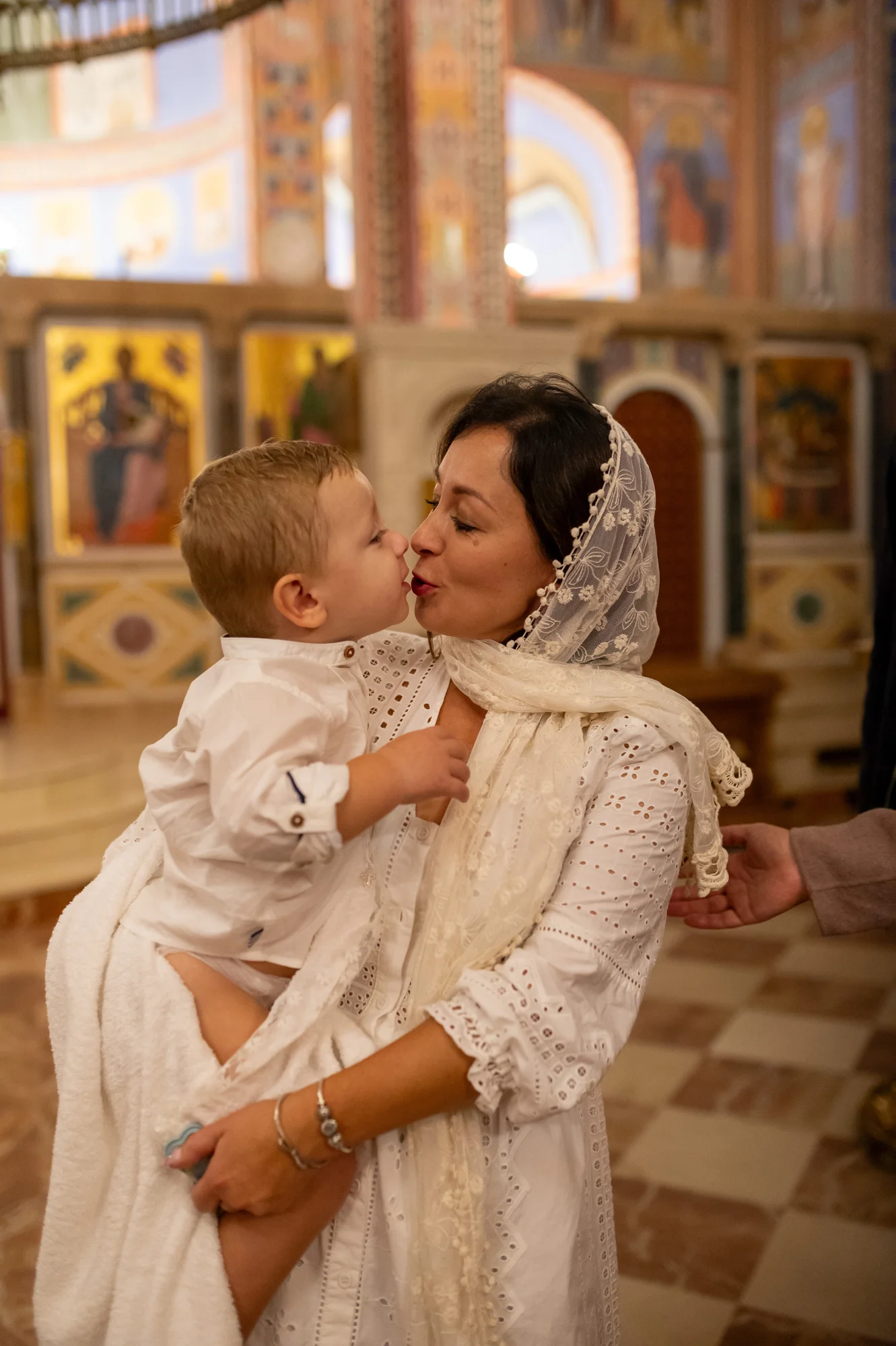Madre con velo blanco besando a su bebé en brazos en una iglesia ortodoxa tras el bautizo