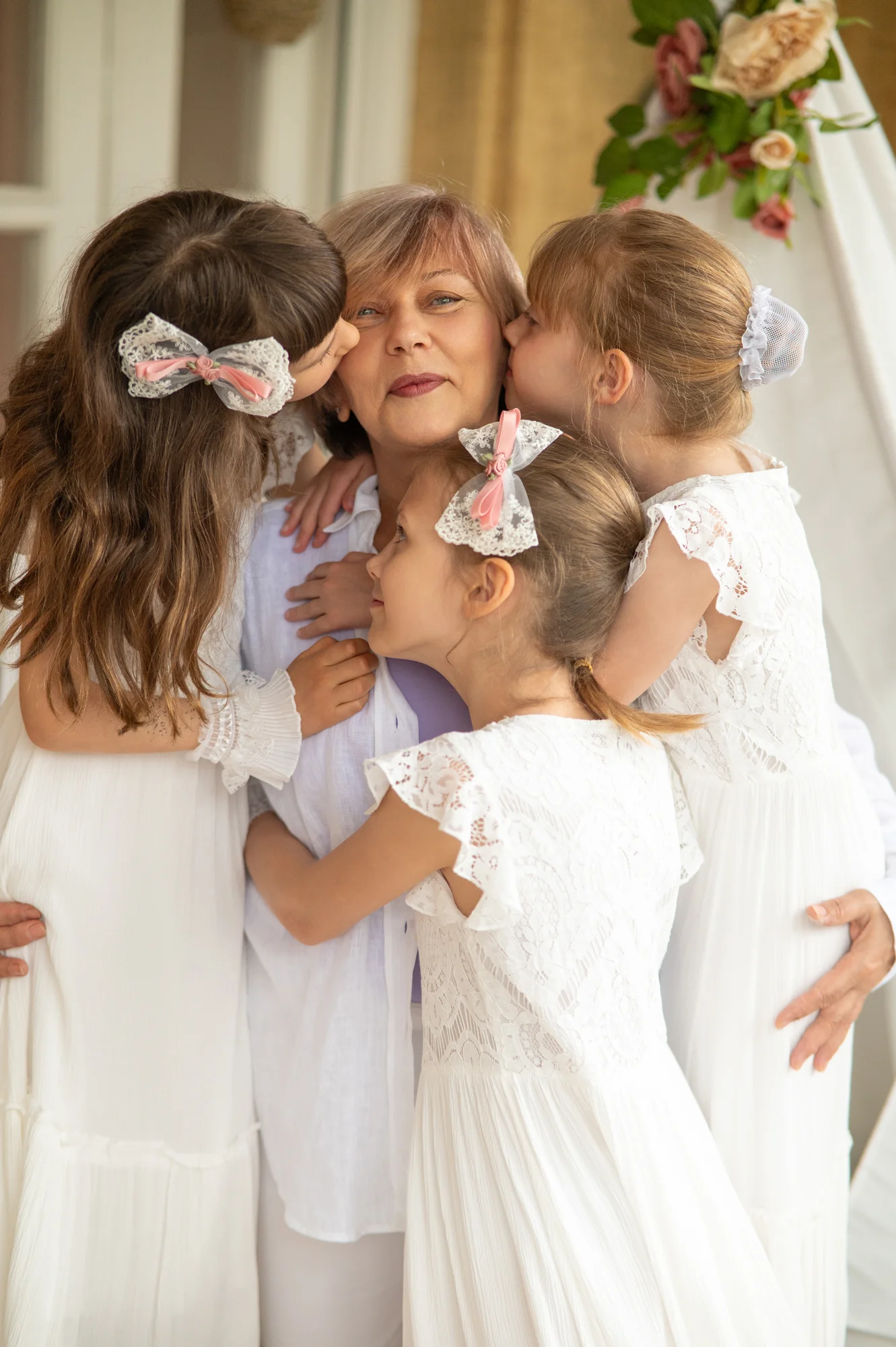 Abuela abrazada por sus tres nietas vestidas de blanco en una sesión de fotos familiar