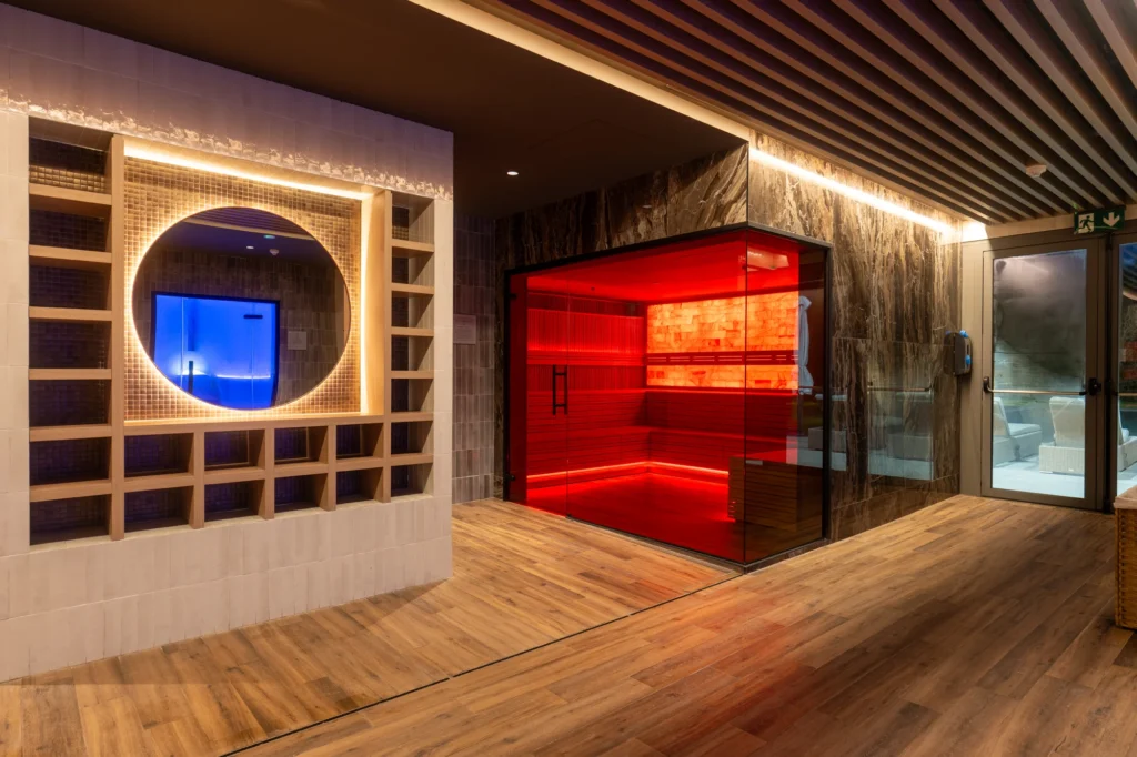 Zona de spa de un club deportivo con sauna de luz roja y mueble iluminado con ventana circular
